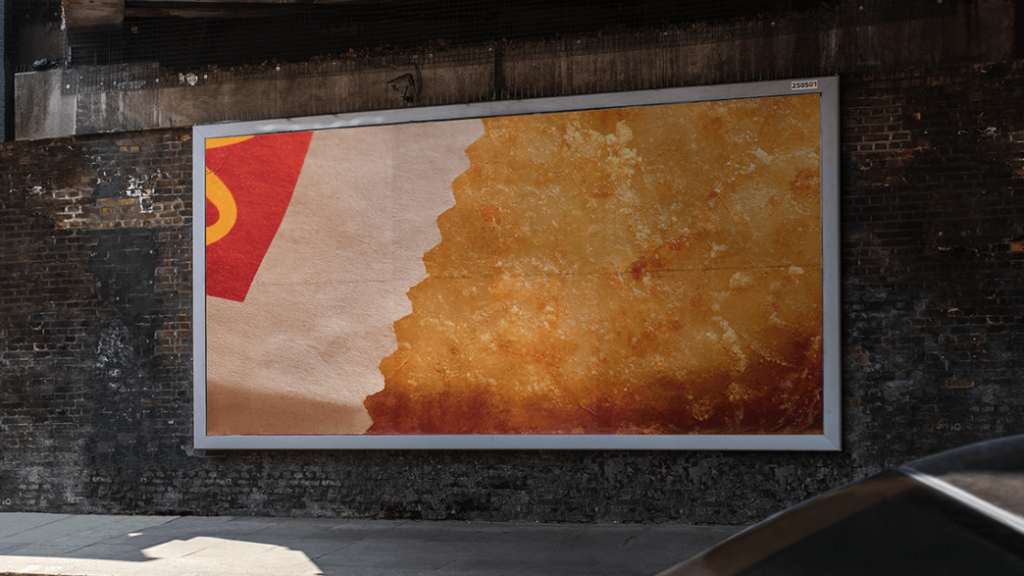 Placa publicitária da marca sem utilizar a logotipo, demonstra parte do produto que se refere e um pequeno pedaço da embalagem.